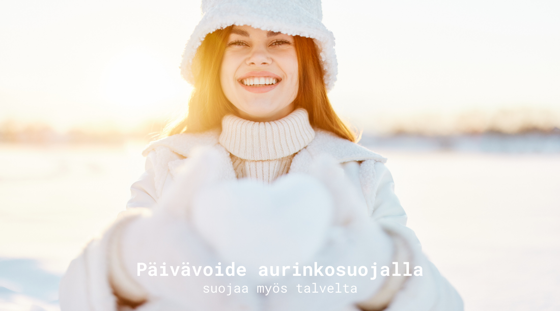 Hymyilevä nainen aurinkoisessa talvimaisemassa näyttää sydämenmuotoista lumipalloa kameralle. Päällään hänellä on valkoinen pörröhattu sekä valkoiset vaatteet.