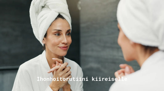 Nainen katsomassa itseään peilistä laitettuaan juur ikasvojenhoitovoiteita. Teksti: ihnohoitorutiini kiireiselle.